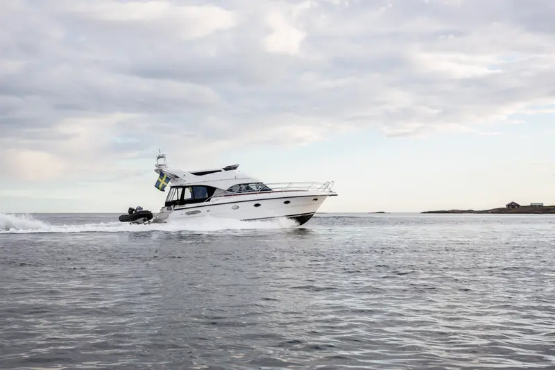 Motorbåt i fart med jollen på badbryggan, skärgården i bakgrunden