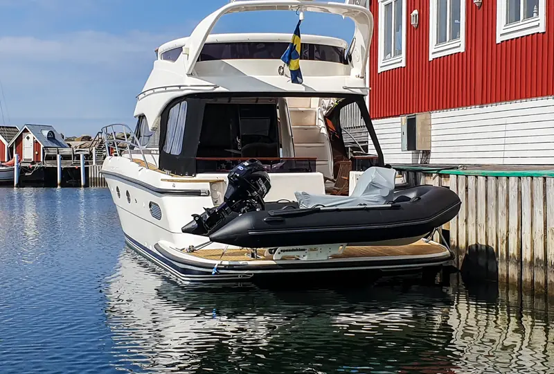 Svart jolle med utombordare tvärs över badbryggan på en motorbåt vid en röd sjöbod